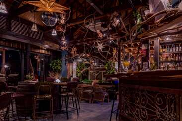 Este acogedor bar cuenta con muebles rústicos de madera, iluminación ambiental y una decoración única con ramas de árbol. Las botellas se alinean en las estanterías, mientras que las frondosas plantas y las lámparas en forma de estrella crean calidez.