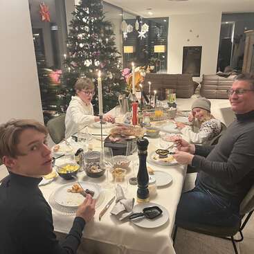 Eine vierköpfige Familie genießt ein festliches Abendessen mit einem schön geschmückten Weihnachtsbaum und Kerzen, die eine warme, gemütliche Atmosphäre in ihrem Haus schaffen.