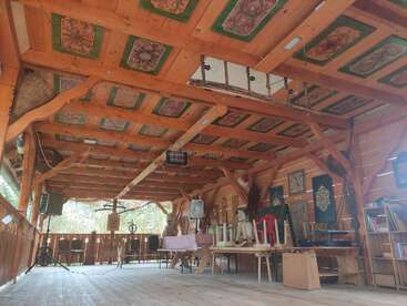 Dieses Bild zeigt einen rustikalen Holzraum mit einer verzierten Decke, Volkskunst, verschiedenen Werkzeugen, Möbeln und traditionellen Gegenständen, die eine gemütliche, kulturelle Atmosphäre schaffen.