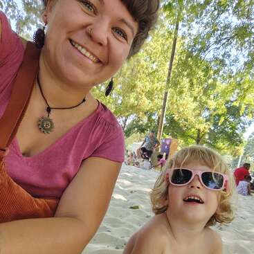 A woman and a young child enjoy a sunny day at the park. The woman smiles brightly, while the child wears pink sunglasses and looks happy.
