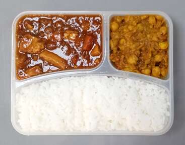 Dieses Bild zeigt ein unterteiltes Essenstablett mit weißem Reis, einem herzhaften braunen Curry mit Gemüse und Fleisch und einem gelben Kichererbsen- oder Linsencurry.