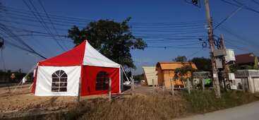 Una tienda roja y blanca se alza en un terreno baldío cerca de una carretera. Cerca hay pequeños edificios de madera, postes eléctricos, cables eléctricos, árboles y vallas.