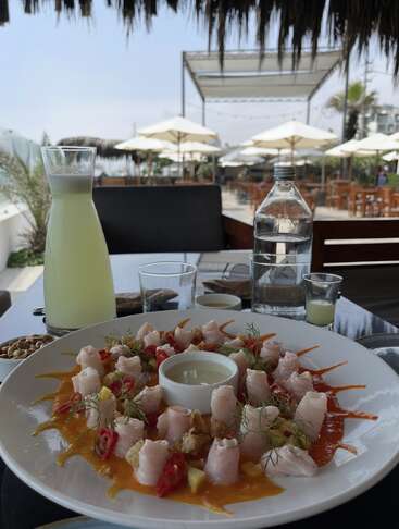 Un magnifique plat de fruits de mer accompagné d'une sauce, de garnitures fraîches et d'un centre de trempage est servi sur une table de restaurant en plein air, accompagné de boissons sous des parasols ensoleillés.