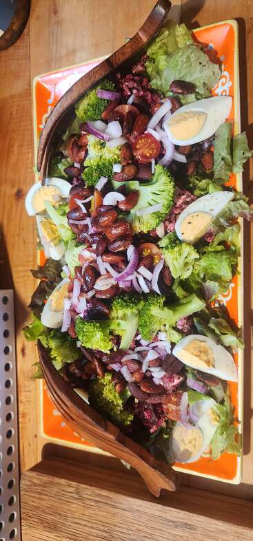 A vibrant salad with mixed greens, broccoli, cherry tomatoes, red onions, roasted almonds, kidney beans, quinoa, and sliced boiled eggs, beautifully presented on an orange platter.