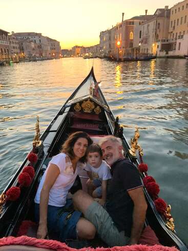 Eine Familie sitzt bei Sonnenuntergang gemeinsam in einer Gondel auf dem Canal Grande in Venedig, umgeben von historischen Gebäuden und sanft leuchtenden Lichtern – ein unvergessliches Erlebnis.