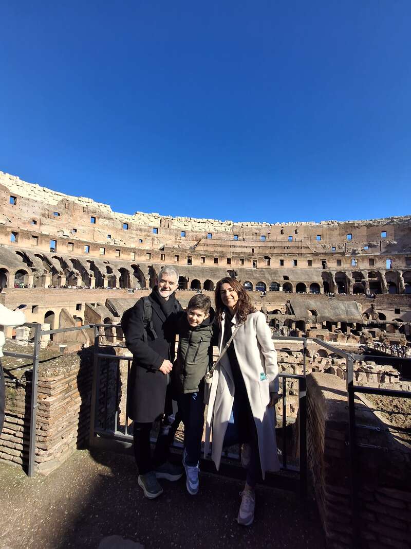 Eine dreiköpfige Familie posiert und lächelt im historischen Kolosseum in Rom unter strahlend blauem Himmel und genießt gemeinsam ihren Sightseeing-Ausflug.