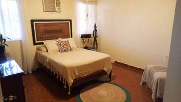 Esse quarto aconchegante tem uma cama de casal com cabeceira estampada, travesseiros decorativos, uma pequena mesa de cabeceira, ar-condicionado, poltrona e muita luz natural.