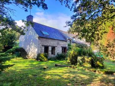 A charming stone cottage with slate roof nestled in a lush, green garden. Surrounded by trees, it exudes tranquility, warmth, and rustic countryside charm.