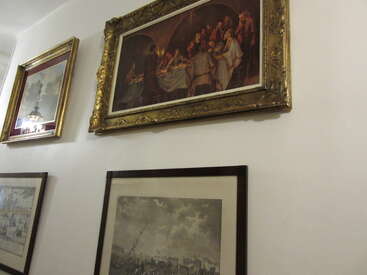 Cette image montre une partie d'un mur sur lequel sont accrochés plusieurs tableaux encadrés, dont une peinture très détaillée et des croquis en noir et blanc, le tout soigneusement disposé à la manière d'une galerie.