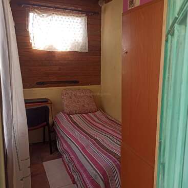 Este pequeño dormitorio cuenta con una cama estrecha con ropa de cama a rayas, una almohada estampada, un armario de madera, una ventana con cortinas y un escritorio compacto con una silla.