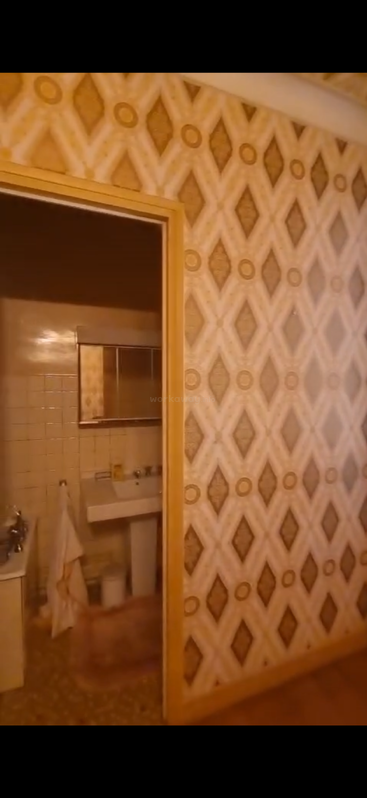Esta imagem mostra um banheiro retrô com papel de parede geométrico e vintage, um espelho, pia, toalhas e paredes revestidas de azulejos. O esquema de cores é principalmente amarelo e marrom.
