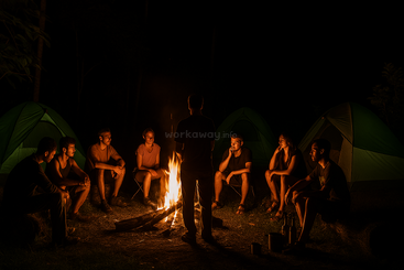 Eine Gruppe von Freunden sitzt nachts um ein glühendes Lagerfeuer, umgeben von grünen Zelten, erzählt sich Geschichten und genießt die friedliche, warme Atmosphäre der Natur.