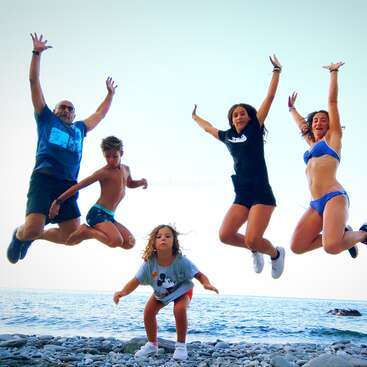 L'image représente une famille joyeuse de cinq personnes sautant sur une plage rocheuse, l'océan et le ciel servant de toile de fond sereine.