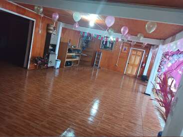 Ein festlicher Raum mit Holzböden und Wänden, die mit rosa, lila und weißen Luftballons geschmückt sind. Von der Decke hängen Banner, die auf eine Feier vorbereiten.