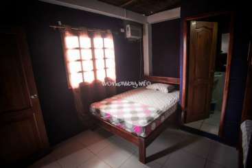 The image depicts a dimly lit bedroom with a bed, mirror, and closet, featuring a white and pink polka dot bedspread and a window with a pink curtain.