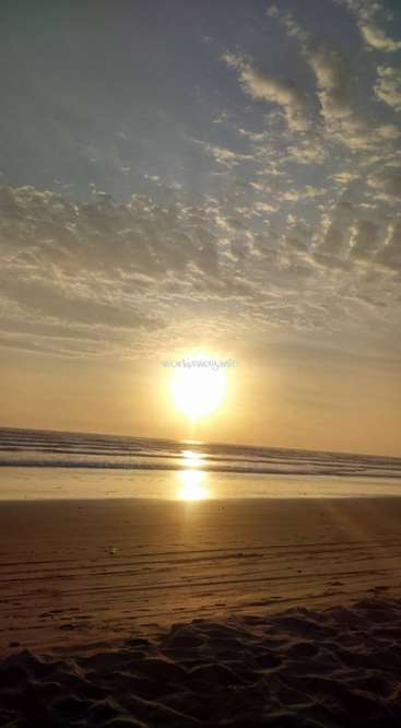 The image depicts a serene beach scene at sunset, with the sun setting over the ocean, creating a warm and peaceful atmosphere.