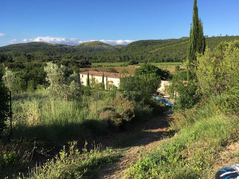 La imagen representa un sereno paisaje rural con un edificio blanco, frondosos árboles y ondulantes colinas bajo un cielo azul despejado, que evoca una sensación de tranquilidad.