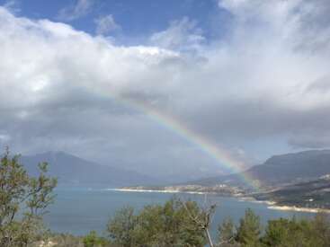 L'image représente un paysage serein avec un arc-en-ciel au-dessus d'une étendue d'eau, des montagnes en arrière-plan et un ciel nuageux.