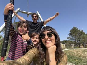 Un grupo de cuatro personas al aire libre en un día soleado, sonriendo y posando para hacerse un selfi. Dos niños y dos adultos disfrutando juntos de un momento de diversión.