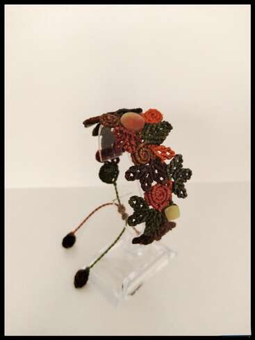 A handmade bracelet featuring intricate macrame knots in earthy tones, adorned with beads and floral designs. The adjustable cord ends in small, crocheted balls. Elegant and rustic.