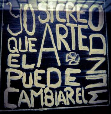 This image features hand-painted, bold white letters on a dark background, saying in Spanish: "Yo sí creo que el arte puede cambiar el mundo."