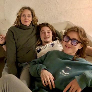 Drei Menschen sitzen eng beieinander auf einem gemütlichen Sofa. Sie wirken entspannt und glücklich und genießen die gemeinsame Zeit in einem warmen, sanft beleuchteten Raum.
