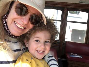 Das Bild zeigt eine Frau und ein Kind in einem Bus, die für ein Selfie posieren, wobei die Frau einen Hut und eine Sonnenbrille trägt.