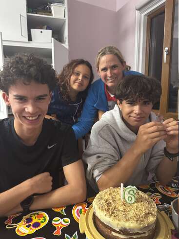 Quatre personnes sont réunies autour d'une table, le sourire aux lèvres. Devant elles se trouve un gâteau orné d'une bougie en forme de « 6 », ce qui laisse supposer qu'il s'agit d'une fête, peut-être un anniversaire. L'ambiance est festive.