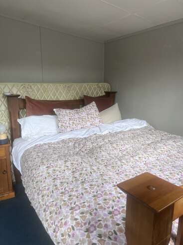 A cozy bed with floral bedding, brown and white pillows, and a wooden headboard. Nightstand with a lamp beside it, set in a minimalist gray room.