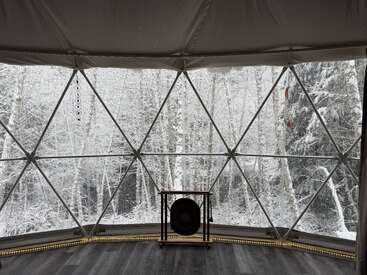 El acogedor interior de la cúpula geodésica ofrece vistas a un bosque nevado a través de claras ventanas triangulares. Un gong y adornos colgantes añaden un ambiente tranquilo y meditativo al interior.