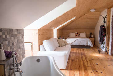 La imagen muestra una acogedora habitación con cama, mesa y sillas, una gran ventana y una chimenea, que transmite una sensación de comodidad y relajación. La habitación está bien iluminada y es acogedora.