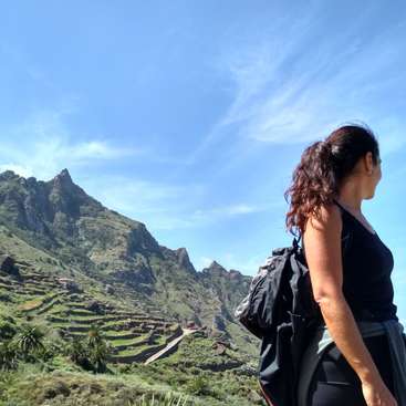 The image depicts a woman gazing at a mountainous landscape, with terraced fields and a blue sky in the background, showcasing a serene natural setting.