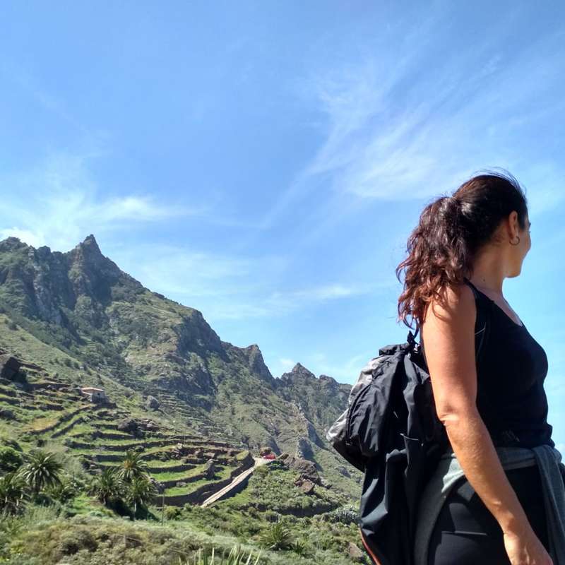 The image depicts a woman gazing at a mountainous landscape, with terraced fields and a blue sky in the background, showcasing a serene natural setting.