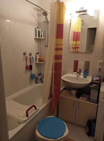 The image depicts a compact bathroom with a bathtub, sink, toilet, and shower, featuring white tiles and a red and yellow striped shower curtain.