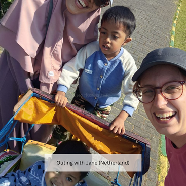 Cuatro personas, entre ellas dos mujeres sonrientes y dos niños pequeños, disfrutan de un día soleado al aire libre. Un niño está sentado en un carrito, todos parecen alegres y felices.
