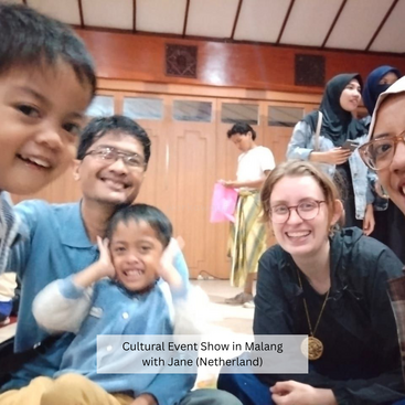 Un grupo de sonrientes adultos y niños posan juntos en el interior de un animado acto cultural en Malang, con Jane de Holanda, disfrutando del momento.