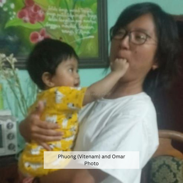 Una mujer sostiene a un niño pequeño vestido de amarillo. El niño pone juguetonamente la mano en la boca de la mujer. Ambos parecen relajados en un ambiente hogareño.