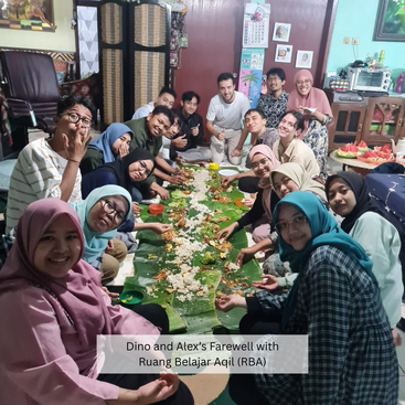 Un alegre grupo se reúne en torno a un banquete de hojas de plátano, compartiendo comida con sonrisas y risas para la despedida de Dino y Alex en Ruang Belajar Aqil (RBA).