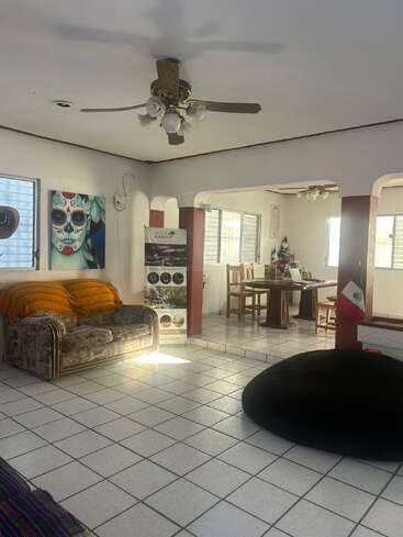 Essa aconchegante sala de estar tem piso de azulejos, ventilador de teto, arte colorida, um sofá com cobertor, uma área de jantar e uma bandeira mexicana como decoração.