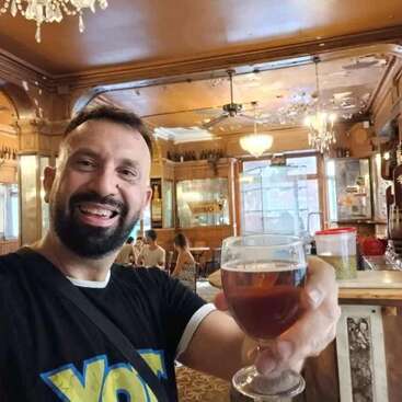 The image depicts a man taking a selfie in a bar, holding a glass of beer, with a warm and inviting atmosphere, featuring wood paneling and chandeliers.