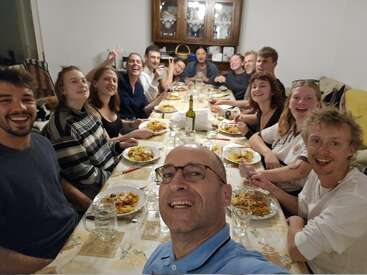 Un groupe de personnes se réunit autour d'une table à manger pour prendre un repas ensemble. Elles sont souriantes, partagent la nourriture, les rires et la bonne compagnie dans un cadre confortable.