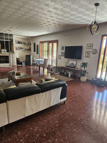This spacious living room features a black-and-white sofa, red marble floors, a TV, coffee table, fireplace, dining area, bookshelf, plants, and abundant natural light.
