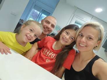A happy family of four, including two adults and two children, smiles together at a table in a bright, modern kitchen, enjoying their time together.