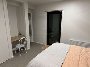 Une chambre confortable avec un lit bien fait, un petit bureau avec une chaise, un radiateur, une porte donnant sur l'extérieur, des murs neutres et une décoration simple pour plus de confort.