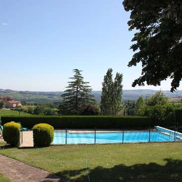Das Bild zeigt einen ruhigen Hinterhof mit einem Pool, umgeben von üppigem Grün und einer malerischen Landschaft vor einem klaren blauen Himmel.