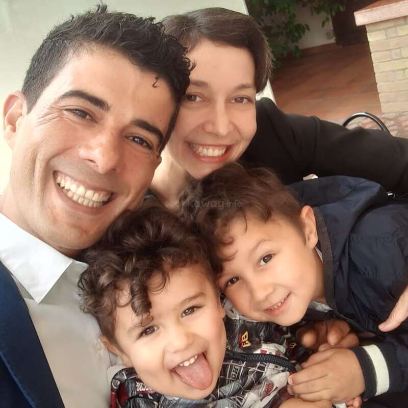 A imagem mostra uma família de quatro pessoas posando para uma selfie, com duas crianças em primeiro plano e os pais abraçando-as por trás.