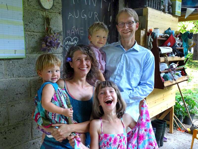 Eine glückliche fünfköpfige Familie posiert zusammen und lächelt herzlich. Im Hintergrund sind eine Kreidetafel mit Schrift und Herzen, Regale und hängender Lavendel zu sehen. Lässige, fröhliche Atmosphäre.