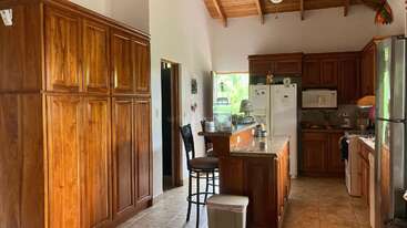 Esta cocina cuenta con ricos armarios de madera, una isla central, electrodomésticos de acero inoxidable, un taburete de bar, nevera blanca, suelos de baldosas y un techo inclinado de madera. Luminosa y acogedora.