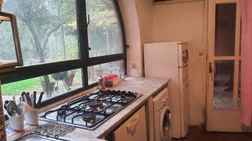 Cette cuisine confortable dispose d'une grande fenêtre cintrée, d'une cuisinière à gaz, d'appareils électroménagers, d'un lave-linge, d'un réfrigérateur, d'ustensiles et d'une porte donnant sur le jardin.