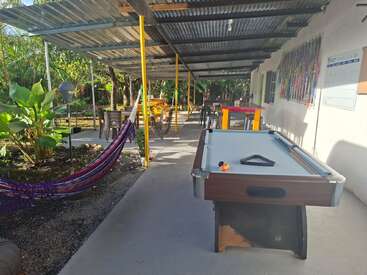Une terrasse extérieure couverte équipée d'un billard, d'un hamac, de tables et de chaises ; entourée de plantes et de verdure, elle offre un espace de détente accueillant et propice à la détente.